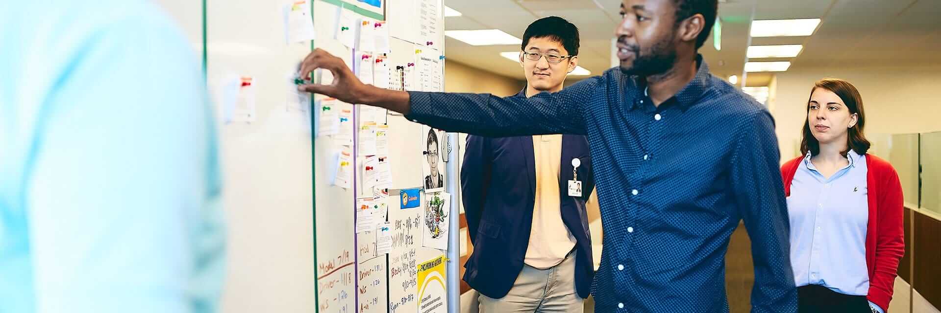 Penn Mutual employees standing at a white board, updating the sprint status.