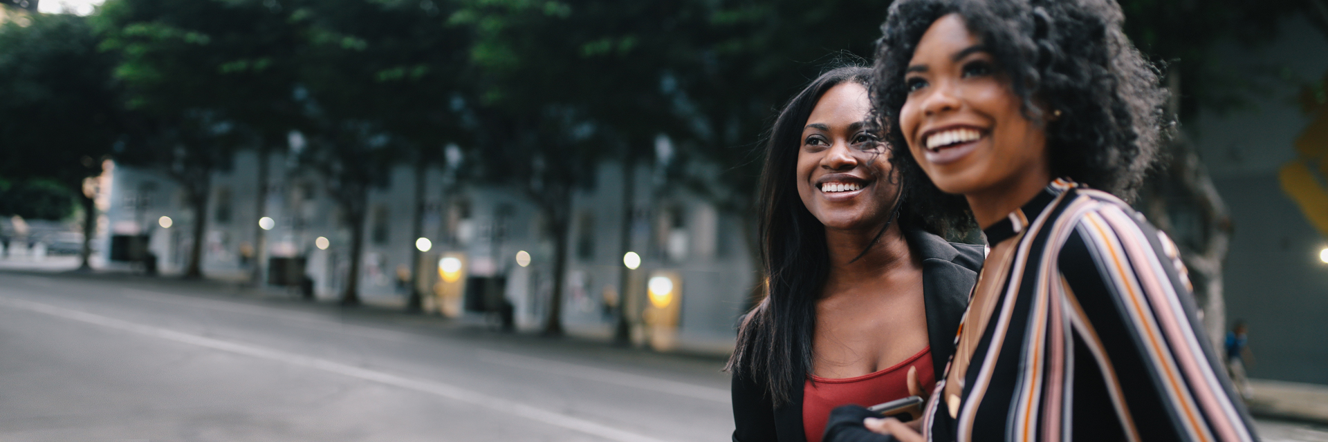 Two smiling black women standing on a street.
