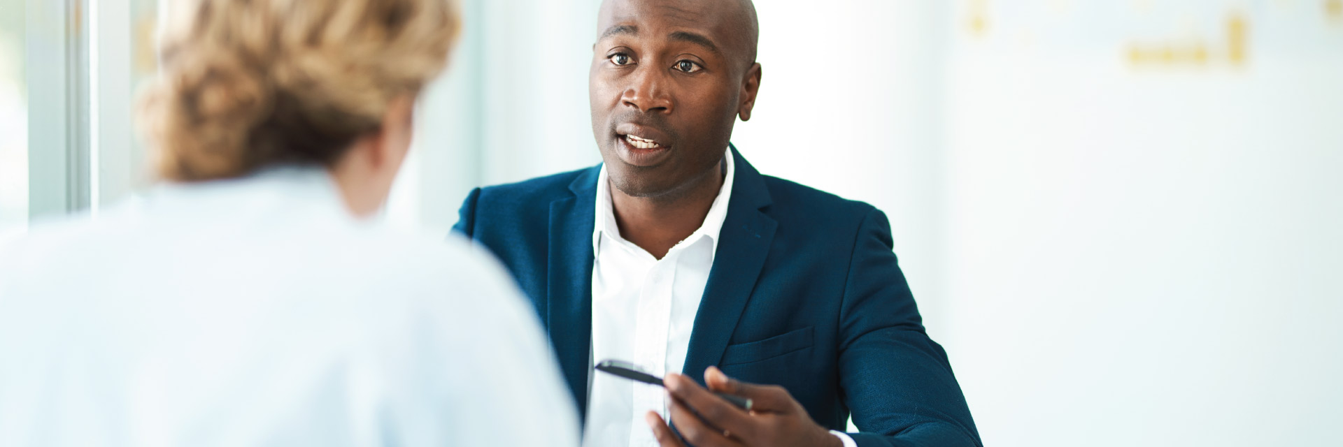 A man in a suit engages in a conversation with a woman who sits across from him.