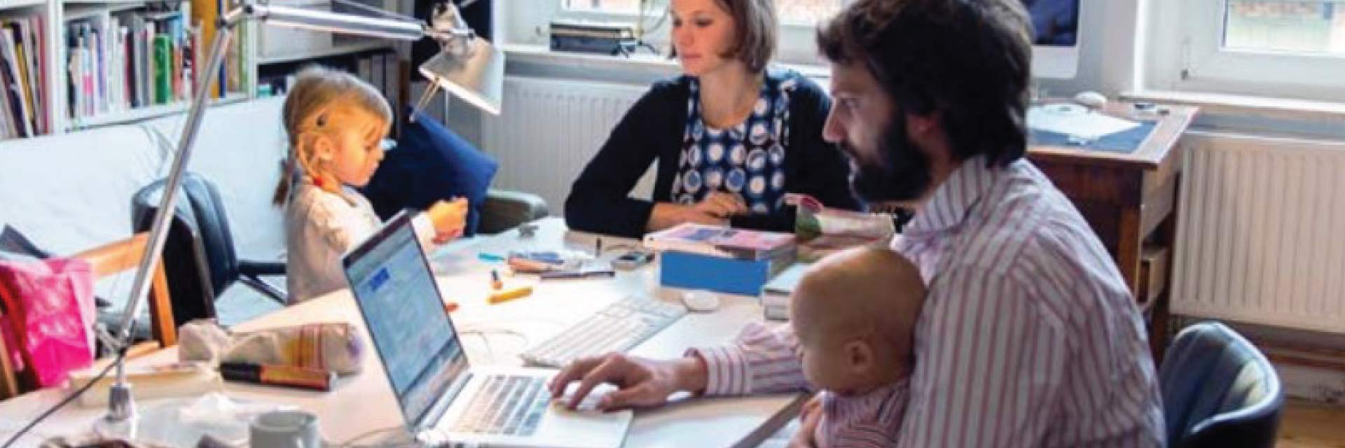 A family consisting of a man, woman, and two young kids all work at a large table.