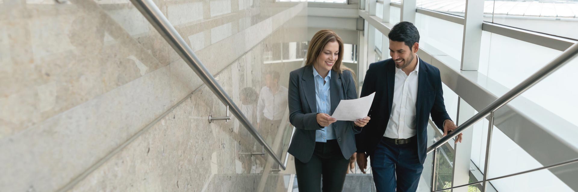 Two financial professionals review a document while walking up a flight of stairs.