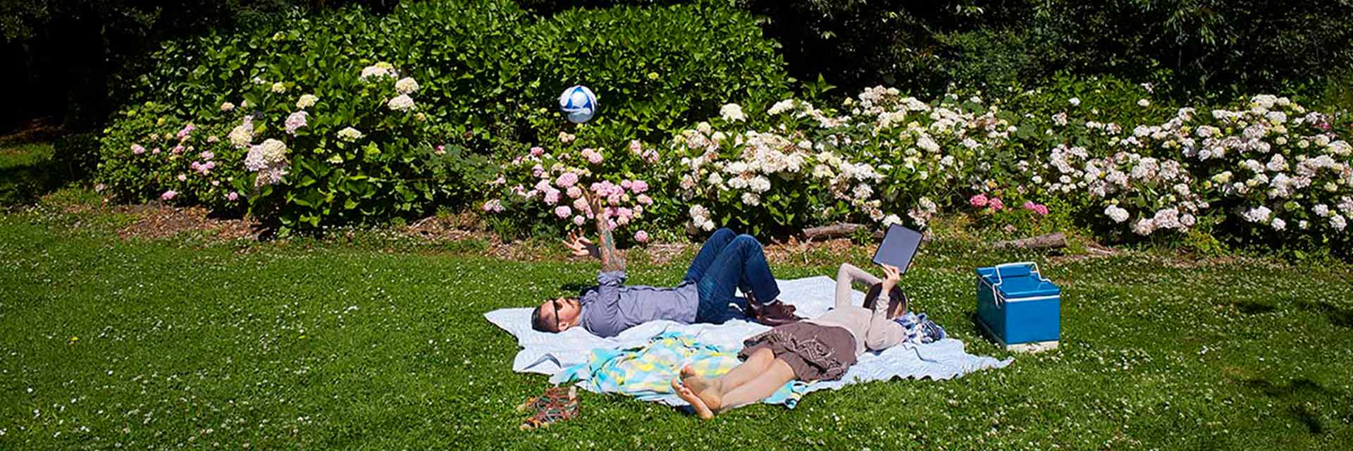 A man and woman lay on a picnic blanket in a park.